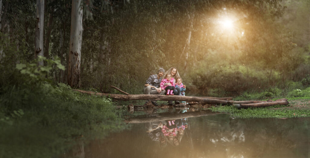 זוג הורים עם שתי הבנות שלהם יושבים על גזע עץ בטבע